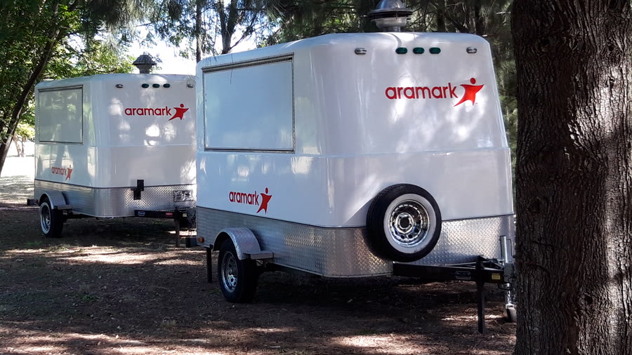 Dos trailers de OCHO ploteados con la gráfica de Aramark, blancos con el logotipo en rojo, en un pinar